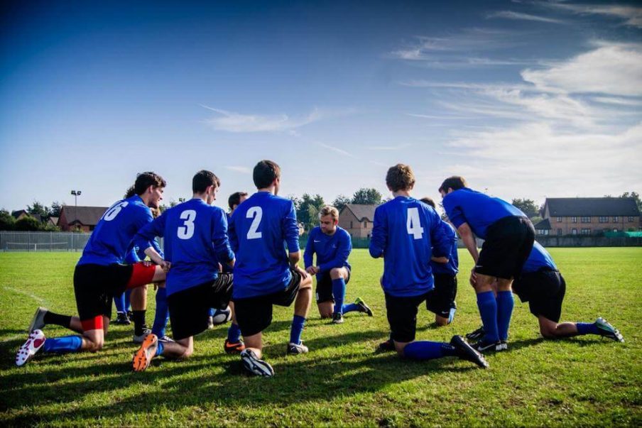 a soccer team in blue uniforms takes a knee to huddle before a game.